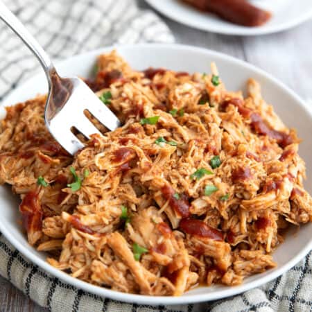 Keto BBQ Shredded Chicken piled up in a white bowl with a serving fork digging into it.