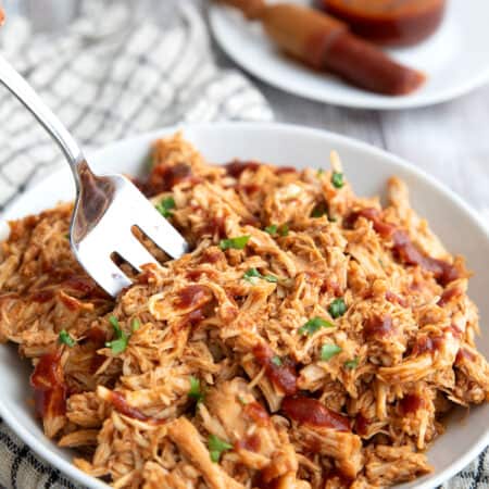 Keto BBQ Shredded Chicken piled up in a white bowl with a serving fork digging into it.