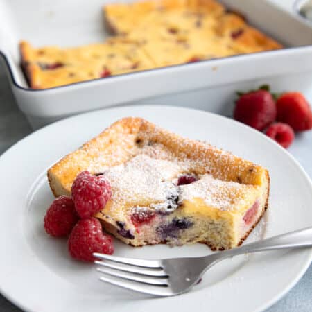A slice of Keto Cottage Cheese Breakfast Bake with three raspberries and a fork on a white plate.