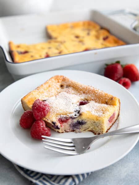 A slice of Keto Cottage Cheese Breakfast Bake with three raspberries and a fork on a white plate.