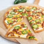 Jalapeño Popper Pizza with fathead dough crust on a parchment lined cutting board with a slice cut out of it.