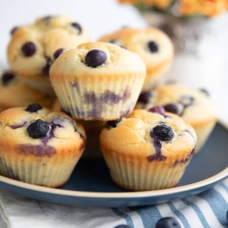 Keto Blueberry Muffins piled up on a blue plate over a striped blue and white napkin.