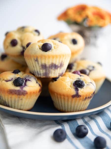 Keto Blueberry Muffins piled up on a blue plate over a striped blue and white napkin.