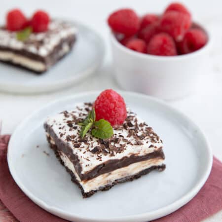 Two slices of Keto Sex In A Pan on white plates with a bowl of fresh raspberries.