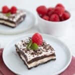 Two slices of Keto Sex In A Pan on white plates with a bowl of fresh raspberries.
