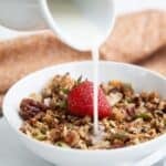 Titled image for Air Fryer Keto Granola in a white bowl with almond milk being poured over it.