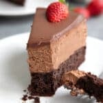 Close up shot of a slice of Keto Chocolate Mousse Cake on a white plate, with a forkful taken out of it.