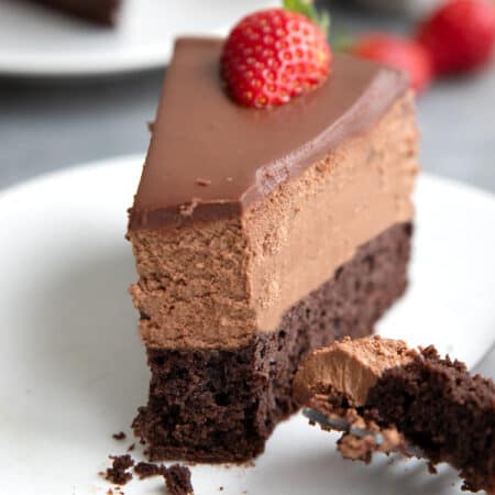 Close up shot of a slice of Keto Chocolate Mousse Cake on a white plate, with a forkful taken out of it.