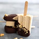 Three keto peanut butter popsicles in a stack with one in front on its end, on a gray concrete table.