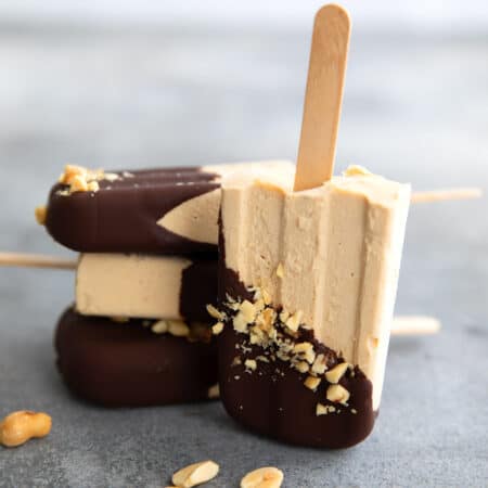 Three keto peanut butter popsicles in a stack with one in front on its end, on a gray concrete table.