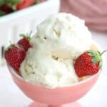 Close up shot of two scoops of keto vanilla ice cream in a pink ice cream dish, with three fresh strawberries.