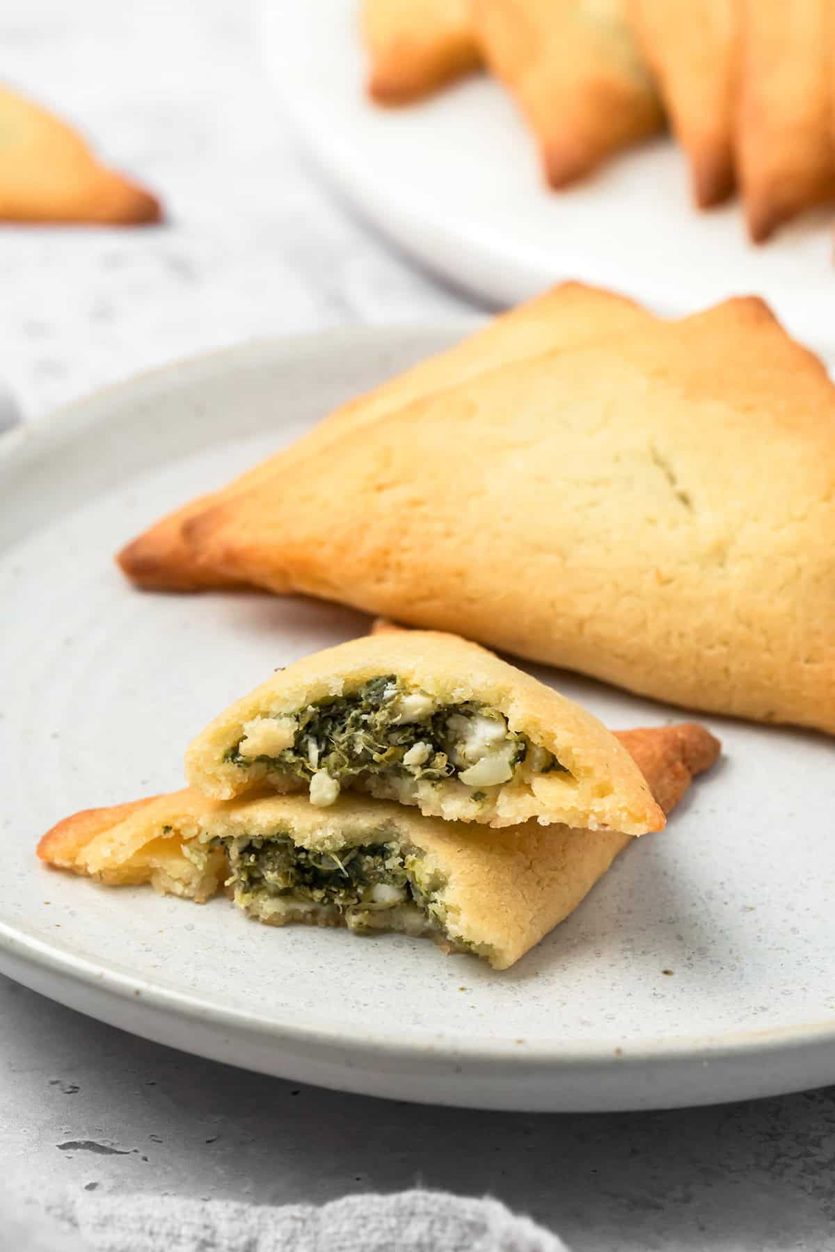 Keto Spanakopita arranged on a white plate with one of the pastries broken open to show the inside.