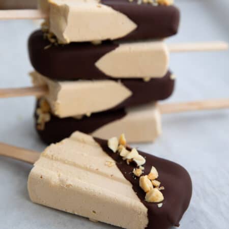 A stack of Keto Peanut Butter Popsicles dipped in chocolate, with one lying in front.