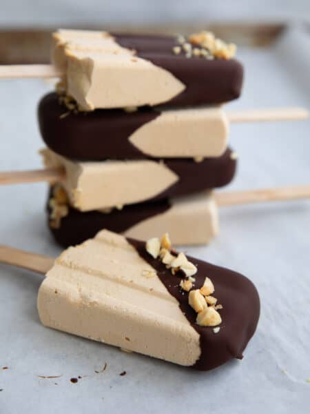 A stack of Keto Peanut Butter Popsicles dipped in chocolate, with one lying in front.