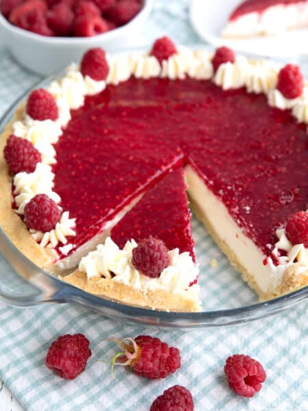 Keto Raspberry Cream Pie in a glass pie plate over a blue and white gingham napkin.