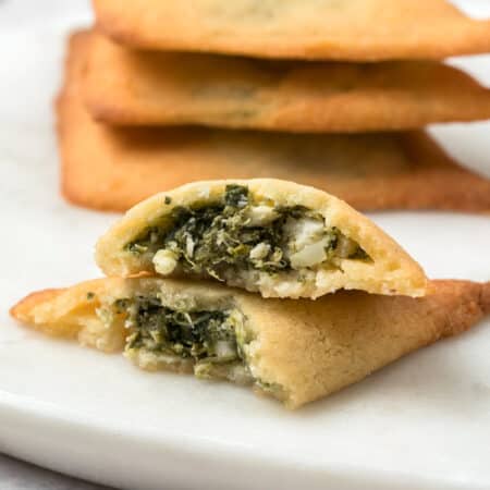 Keto Spanakopita broken open on a white plate with a stack of more savory pastries in the background.