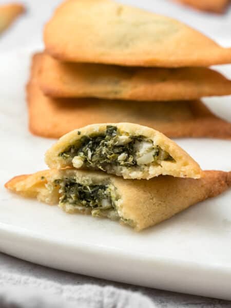 Keto Spanakopita broken open on a white plate with a stack of more savory pastries in the background.