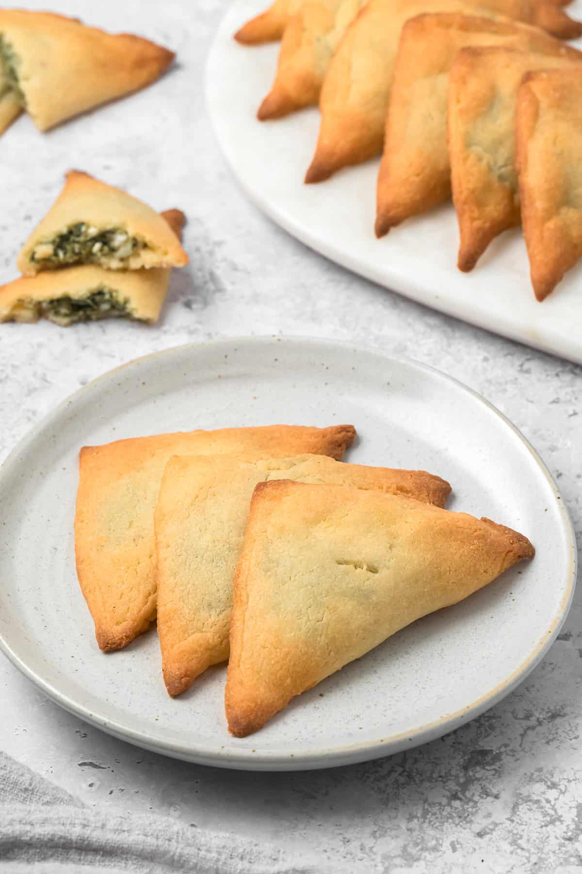 Three Keto Spanakopita arranged on a white plate, on a concrete table top.