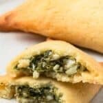Titled image of keto spanakopita broken open to show the inside, on a white plate with more pastries in the background.