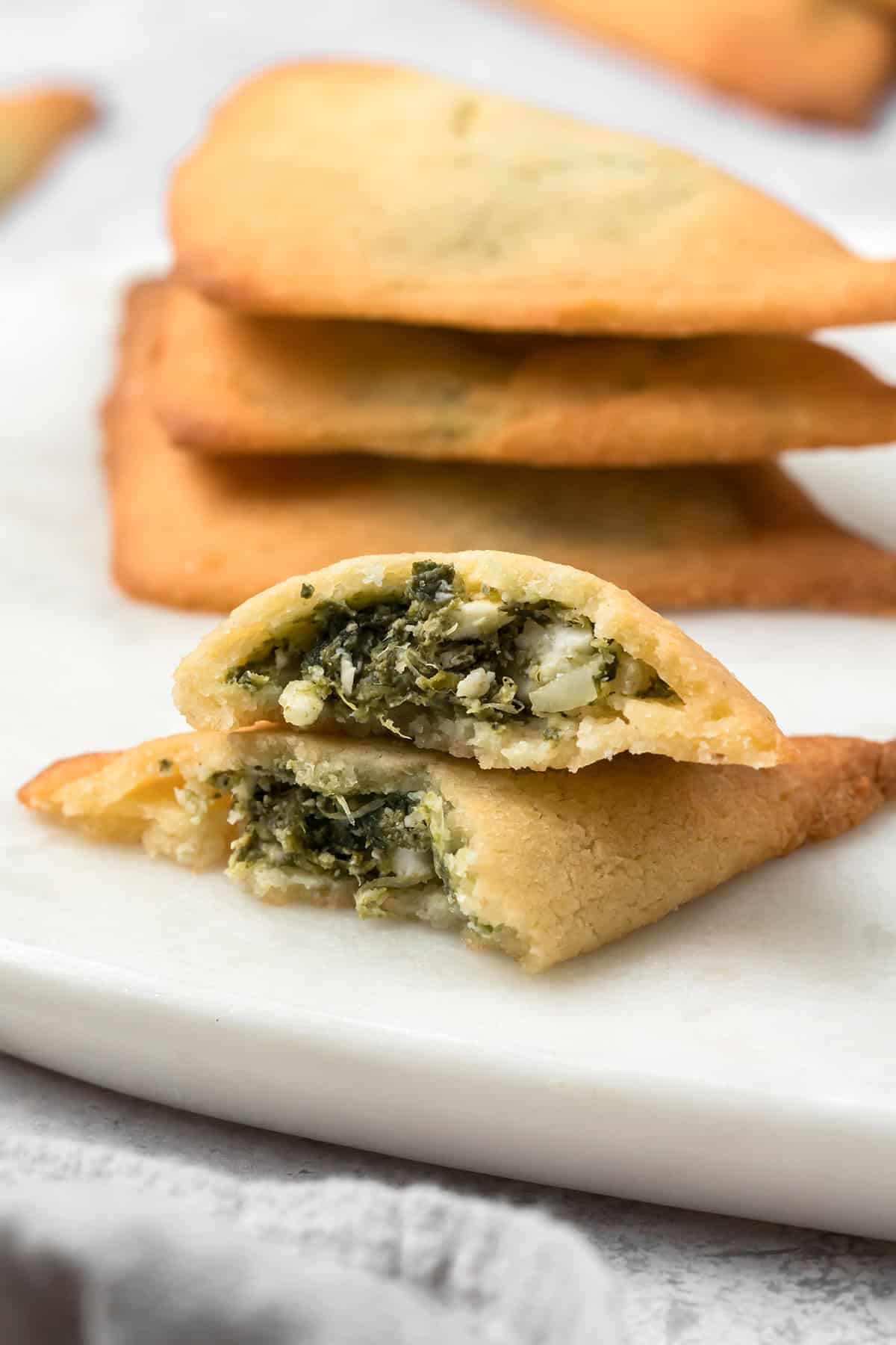 Keto Spanakopita broken open on a white plate with a stack of more savory pastries in the background.