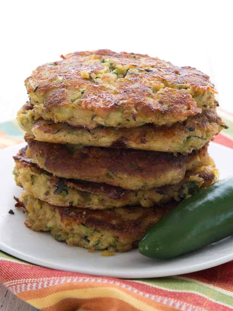 Close up shot of a stack of keto zucchini fritters with a jalapeño pepper on a white plate, over a colorful striped napkin.