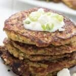 Titled image of a stack of keto zucchini fritters on a white plate with a dollop of sour cream and some green onions sprinkled on top.
