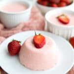 Keto Strawberry Panna Cotta on a white plate with strawberries and more panna cotta in white ramekins in the background.