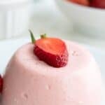 Titled image close up of Keto Strawberry Panna Cotta on a white plate with a sliced strawberry on top.