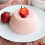Close up image of Keto Strawberry Panna Cotta on a white plate with a sliced strawberry on top.