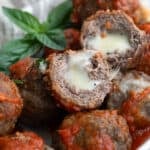 Keto stuffed meatballs piled in a white dish, with one cut open to show the inside.