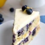 Titled image of a slice of keto lemon blueberry cake on a white plate over a blue napkin.