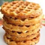 Titled image of a stack of keto cheddar zucchini waffles on a white plate over a colorful striped napkin.