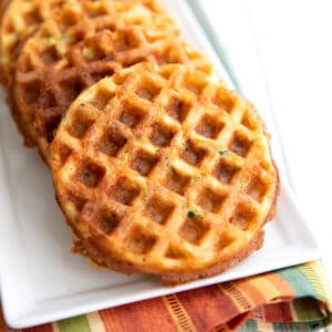 Cheddar zucchini waffles on a white rectangular platter over a striped napkin.