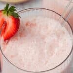 Titled image of a glass of keto strawberry frosted lemonade with half a strawberry on the edge and a glass straw.