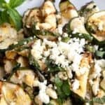 Titled Pinterest pin of a white bowl filled with grilled zucchini and feta, on a white wooden table.