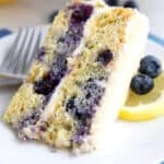 Close up shot of a slice of keto blueberry lemon cake on a white plate over a blue napkin.
