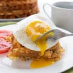 A fork digging into a fried egg on a stack of keto cheddar zucchini waffles.