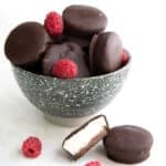Keto Cheesecake Bites piled up in a speckled gray bowl on a white table with two in front.