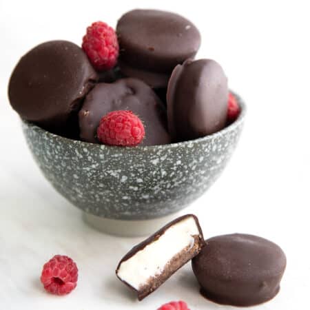 Keto Cheesecake Bites piled up in a speckled gray bowl on a white table with two in front.