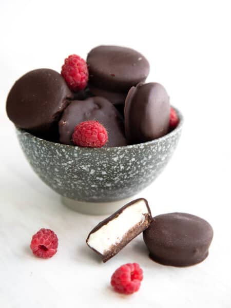 Keto Cheesecake Bites piled up in a speckled gray bowl on a white table with two in front.