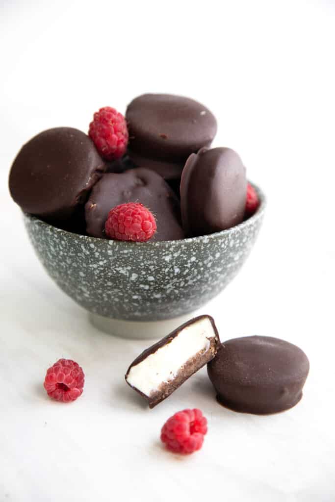 Keto Cheesecake Bites piled up in a speckled gray bowl on a white table with two in front.