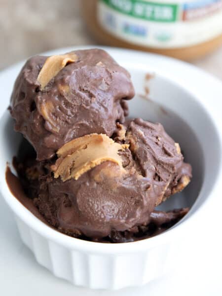 Two scoops of keto chocolate peanut butter ice cream in a white bowl on a white plate.