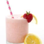 A glass of keto strawberry frosted lemonade with a striped pink straw, a strawberry, and a lemon slice.