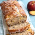 Slices of keto peach bread in front of the loaf on a white platter over a blue gingham napkin.