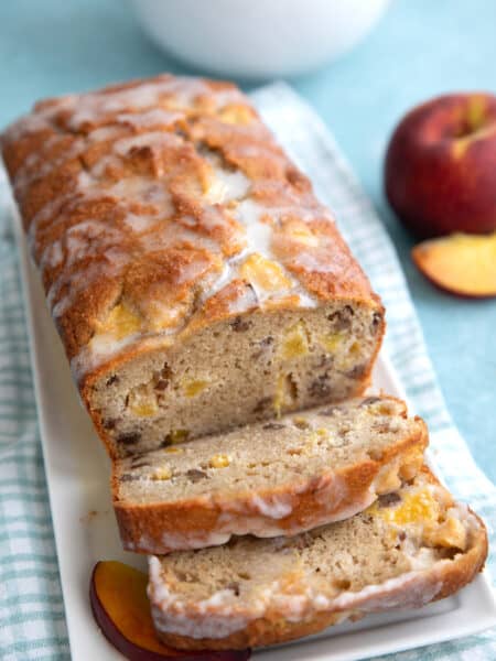 Slices of keto peach bread in front of the loaf on a white platter over a blue gingham napkin.
