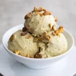 A white bowl with three scoops of keto pistachio ice cream, topped with chopped, salted pistachios.