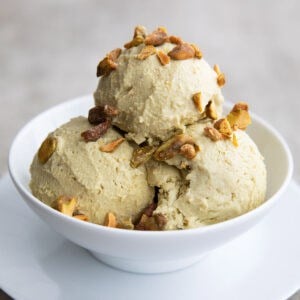 A white bowl with three scoops of keto pistachio ice cream, topped with chopped, salted pistachios.