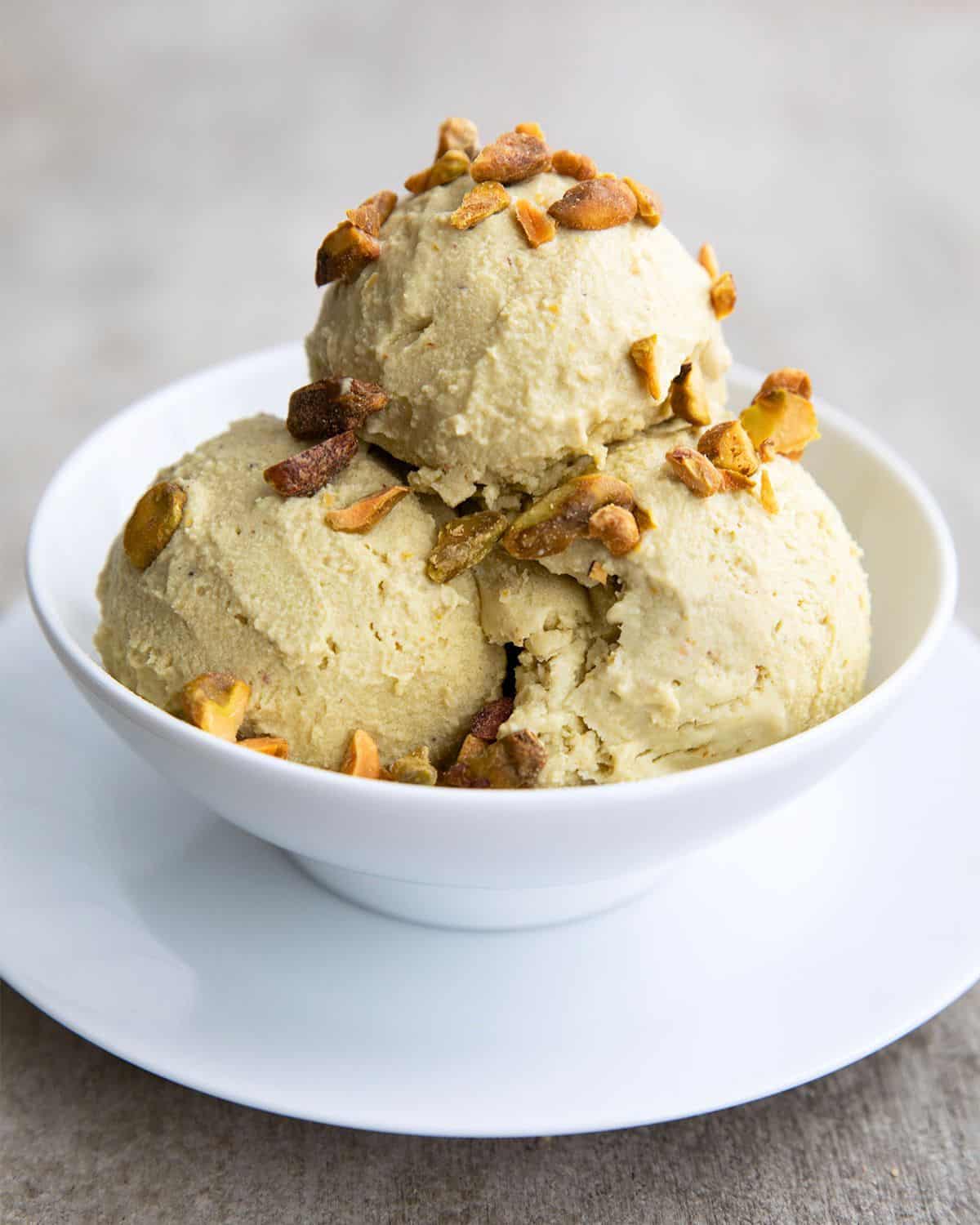 A white bowl with three scoops of keto pistachio ice cream, topped with chopped, salted pistachios.