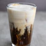 Close up shot of a tall glass filled with iced coffee and protein creamer floating on top.