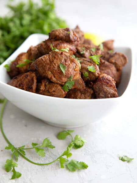 A white bowl filled with Air Fryer Steak Bites on a gray table, with a sprig of cilantro in the foreground.